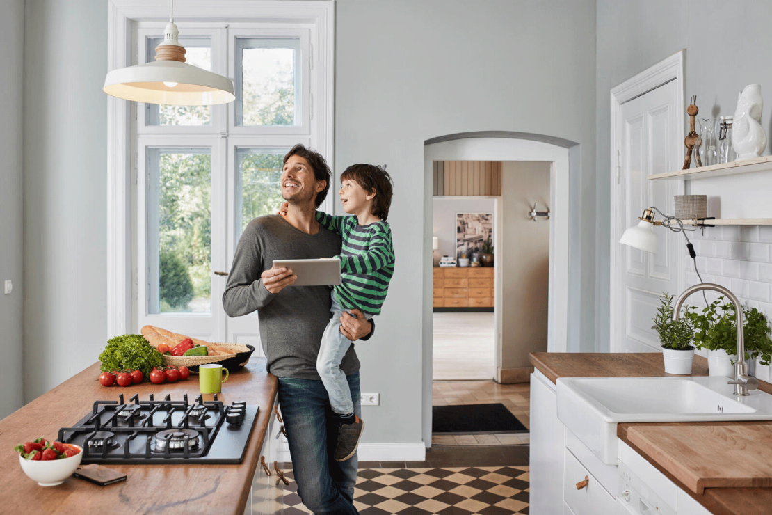 Père utilisant une tablette dans la cuisine, regardant le plafonnier avec son fils dans les bras