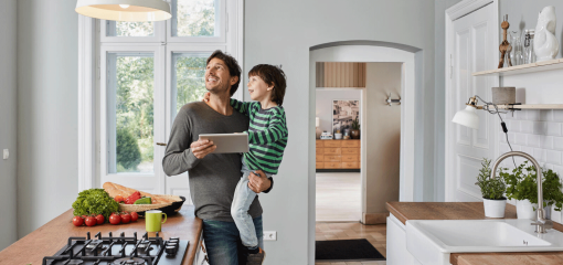 Père utilisant une tablette dans la cuisine, regardant le plafonnier avec son fils dans les bras